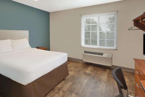 1 dormitorio con cama, ventana y escritorio en WoodSpring Suites St Louis St Charles en St. Charles