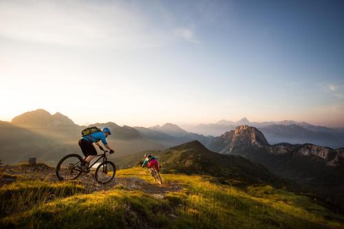 two people riding bikes on a hill with the mountains in the background at das Bergerleben in Sonnenalpe Nassfeld
