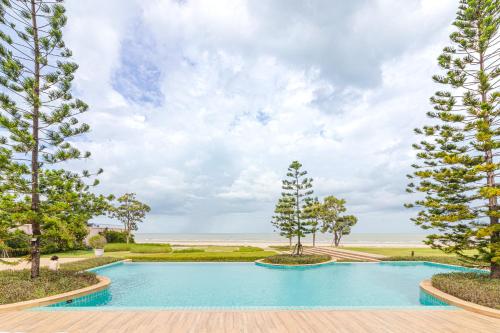 a swimming pool with trees and the beach in the background at Munlihouse Cha-Am Hua-Hin Beach in Cha Am