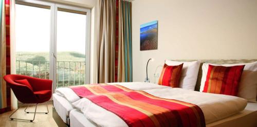 a bedroom with a bed with a red chair and a window at Hapimag Ferienwohnungen Hörnum in Hörnum