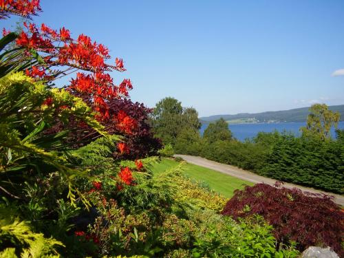 a garden with red flowers and trees and a lake at Loch Ness Lodge in Drumnadrochit