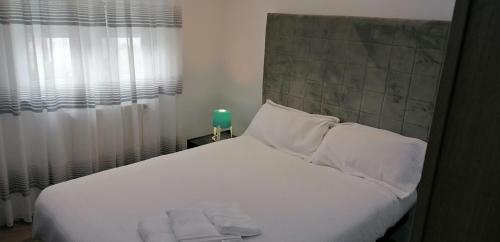 - un lit avec des draps et des oreillers blancs à côté d'une fenêtre dans l'établissement ApartamentoOtero, à Oviedo