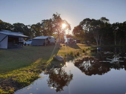 a group of tents and a lake with the sun shining at 1770 Southern Cross Travellers Retreat in Agnes Water