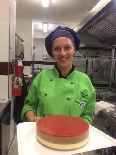 a woman in a kitchen holding a red cake at Eraclea Palace Hotel 4 stelle S in Eraclea Mare
