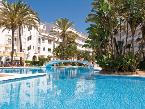 a large swimming pool with palm trees and a bridge at Playa Real in Marbella