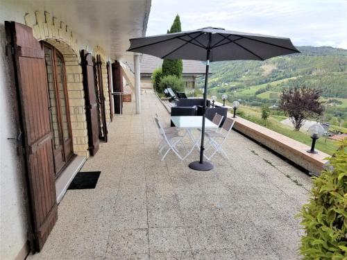 a patio with an umbrella and chairs and a table at Ô Panoragite - Gîte familial in Boëge