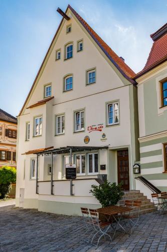 un grande edificio bianco con sedie di fronte di Bistro-Pension Vis-a-Vis a Vohburg an der Donau