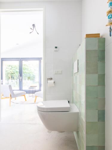 a white bathroom with a toilet and a chair at De Duinlopers- appt Zilt Zand- Strand, duinen en nabij cultuur steden in Castricum