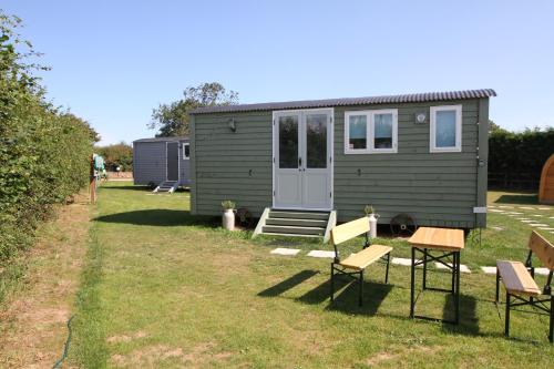 a green tiny house in a yard with chairs at Lanterns Shepherds Huts & Glamping in Happisburgh
