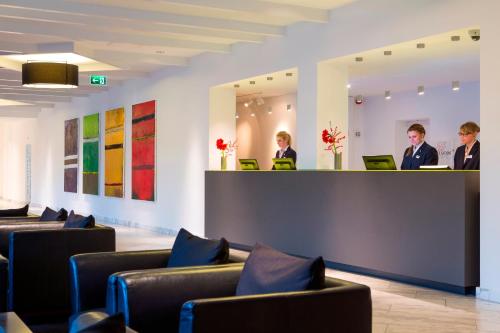 three people standing at a counter in a waiting room at Park Inn by Radisson Lübeck in Lübeck