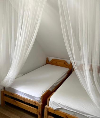 two beds in a room with white curtains at Pipacs in Balatonszárszó