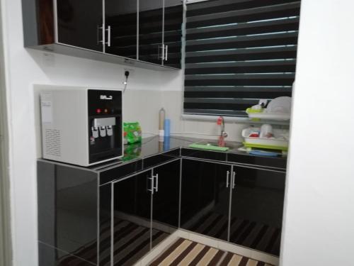 eine Küche mit schwarzen Schränken und einer Mikrowelle in der Unterkunft Amani Apartment Homestay in Malakka