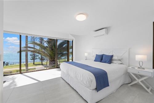 a white bedroom with a bed and a large window at Alexandria Apartments in Alexandra Headland