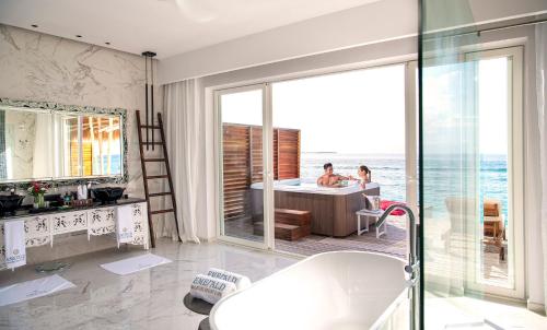 a bathroom with a tub and a table with a view of the ocean at Emerald Maldives Resort & Spa-Deluxe All Inclusive in Raa Atoll