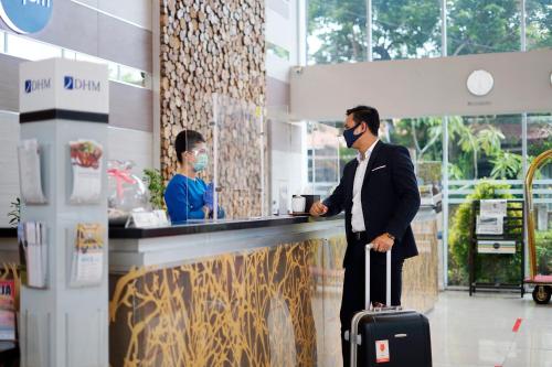 Een man met een masker op en staat met een koffer aan de toonbank. bij Hotel Dafam Pekanbaru in Pekanbaru