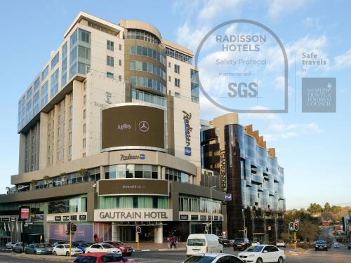 a large building with cars parked in front of it at Radisson Blu Gautrain Hotel, Sandton Johannesburg in Johannesburg