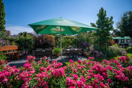 a green umbrella in a garden with pink flowers at Hotel Garni Zur Alten Post in Lembruch