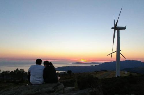 a couple sitting on a rock watching the sunset with a windmill at A Casa de Feli in Muros
