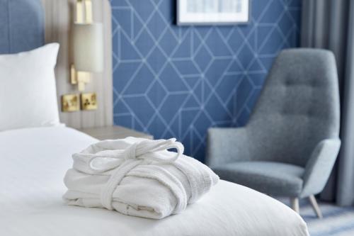a pile of towels sitting on a bed with a chair at Leonardo Royal Southampton Grand Harbour in Southampton