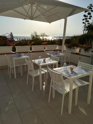 a patio with white tables and chairs and an umbrella at Map Enjoy Rooms in San Vito lo Capo