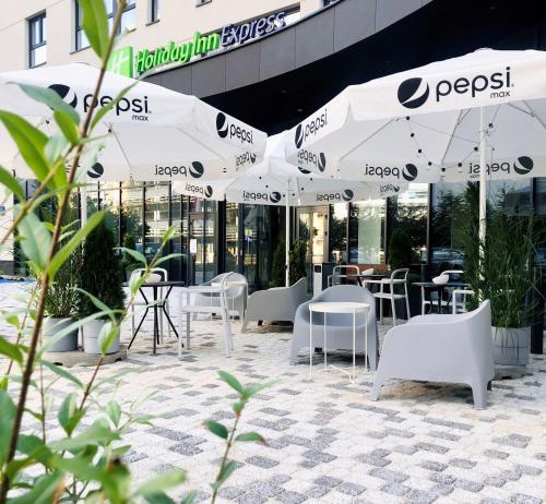 un patio con mesas blancas, sillas y sombrillas en Holiday Inn Express Warsaw - Mokotow, an IHG Hotel en Varsovia