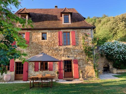 Cette ancienne maison en pierre est dotée de volets rouges et d'une table avec un parasol. dans l'établissement Maison, vue et piscine privée avec ouverture septembre à côté de Sarlat, à Bézenac