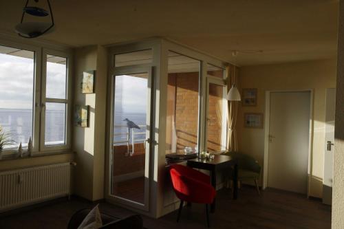 146 Suedstrand Meerblick في فيلهلمسهافن: غرفة بها كرسي احمر وطاولة ونوافذ