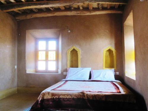 a bed in a room with two windows at Casbah d'hôte La Jeanne Tourisme Ecologique in Boumalne