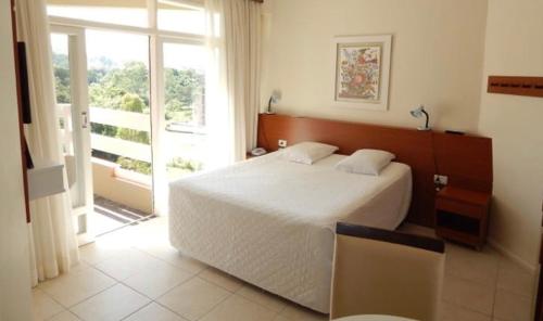 um quarto com uma grande cama branca e uma janela em Flats termais em condomínio Apart Hotel de águas termais em Gravatal