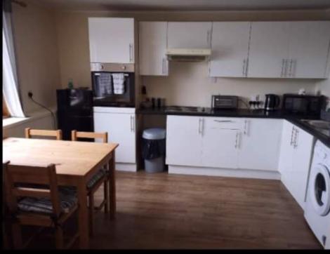 a kitchen with white cabinets and a wooden table with chairs at Panoramic Harbour View Apartment in Oban