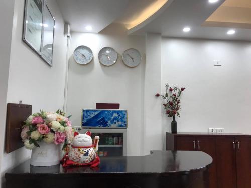 Nhà Nghỉ Hoa Linh - 79 Phố Mía في هانوي: غرفة مع طاولة مع إناء من الزهور والساعات
