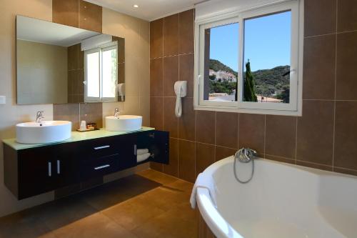 La salle de bains est pourvue de 2 lavabos, d'une baignoire et d'une fenêtre. dans l'établissement Hôtel A Madonetta, à Bonifacio
