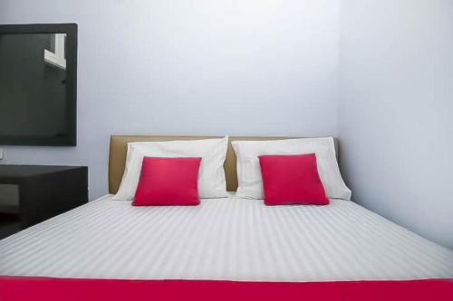 a white bed with two pink pillows and a television at RedDoorz Near Stasiun Lawang in Lawang