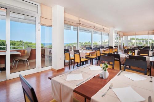 restauracja ze stołami i krzesłami oraz dużymi oknami w obiekcie Hotel Albatros Plava Laguna w Poreču