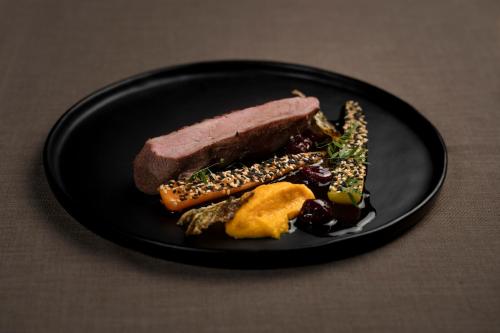 a black plate with a piece of meat and vegetables at Sporthotel am Semmering in Semmering