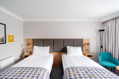 a hotel room with two beds and a blue chair at Holiday Inn Hemel Hempstead M1, Jct. 8 by IHG in Hemel Hempstead