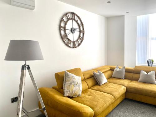 a brown couch in a living room with a clock on the wall at Winter Gardens Service Apartments by Blackpool Service Apartments in Blackpool