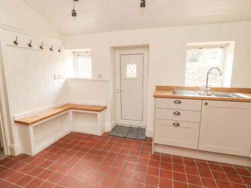 cocina con armarios blancos y suelo de baldosa roja en Hill Top Cottage, en Keighley