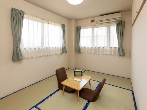 um quarto com uma mesa, cadeiras e janelas em Tabist Business Ryokan Duck Ishinomaki Hebita em Ishinomaki