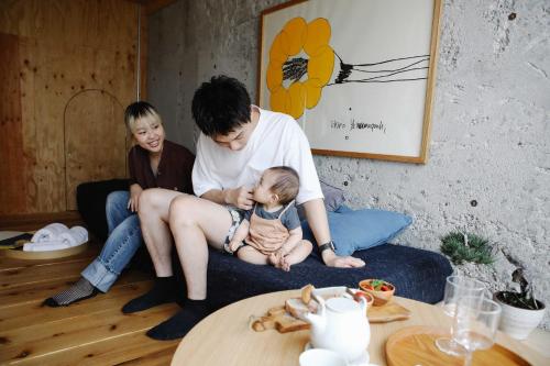 Ein Mann und zwei Frauen sitzen auf einer Couch mit einem Baby in der Unterkunft Sunny Day Hostel in Takamatsu