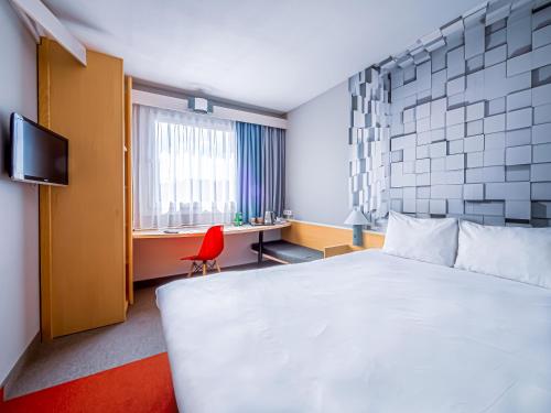 a hotel room with a white bed and a red chair at Ibis Katowice - Zabrze in Zabrze