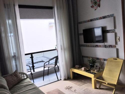 ein Wohnzimmer mit einem Sofa, einem TV und einem Balkon in der Unterkunft Apartamento Enseada in Guarujá