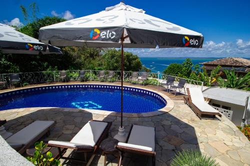 a swimming pool with an umbrella and chairs and a table at Pousada Natureza in Morro de São Paulo