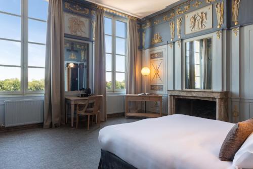 a bedroom with a bed and a fireplace and windows at Hôtel Anne d'Anjou, The Originals Collection in Saumur