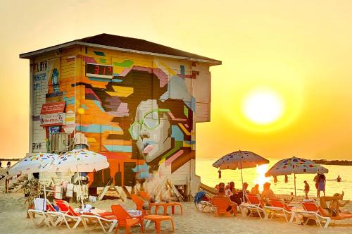 a building on the beach with people sitting under umbrellas at Ben Yehuda Apartments in Tel Aviv