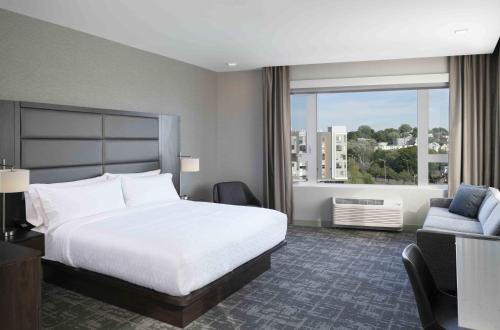 a hotel room with a bed and a couch and a window at Staybridge Suites - Boston Logan Airport - Revere by IHG in Revere