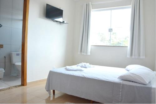 a white bedroom with a bed and a window at Pousada Dom Pedro in Caxambu