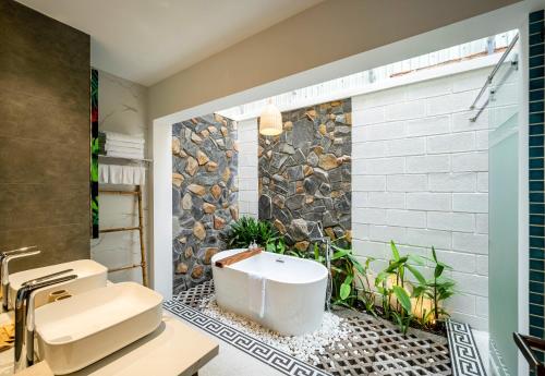 a bathroom with a white tub and a stone wall at The Kila Boutique Hotel in Quy Nhon