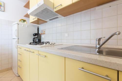 La cuisine est équipée de placards jaunes, d'un évier et d'un réfrigérateur. dans l'établissement Apartmani Manzoni, à Punat