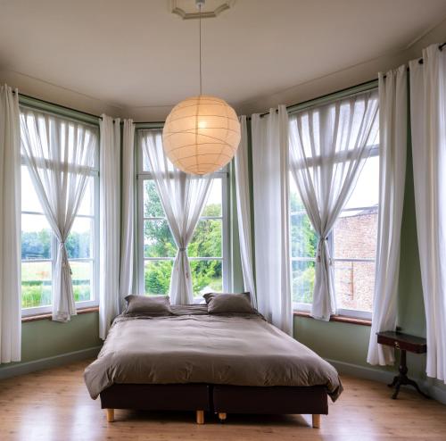 een slaapkamer met een groot bed voor de ramen bij Kasteel Nieuwenhoven in Sint-Truiden